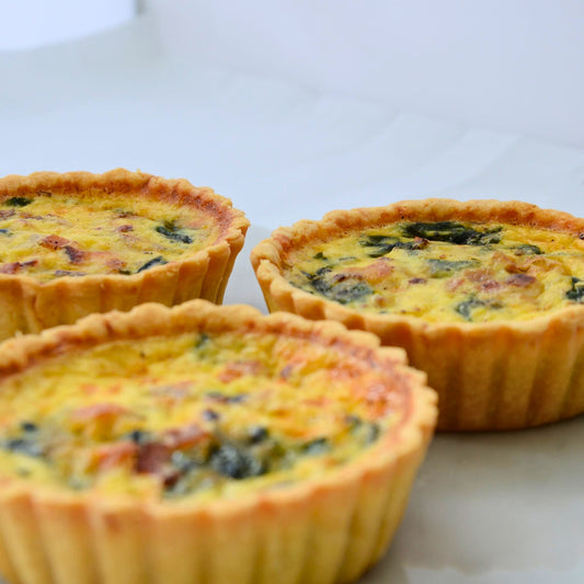 Three single serve Bacon Spinach quiches 10cm arranged on marble board showing golden buttery thin crust and creamy custard top with fresh spinach and crispy bacon Carpina Bakery Singapore