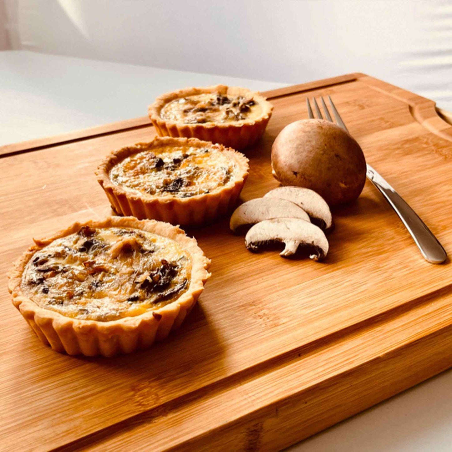 Three single serve mushroom and ham quiches on a wooden board with fresh mushrooms and a fork, 10cm individual size, Carpina Bakery Singapore