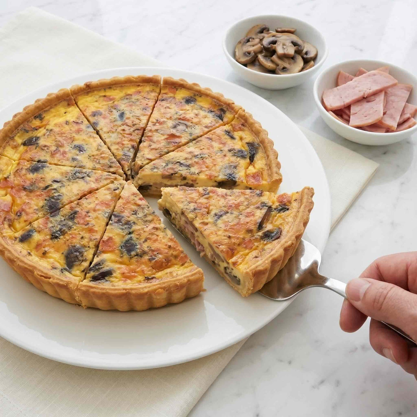 Slice being lifted from 24cm Mushroom and Ham Quiche with a cake server, showing creamy custard interior with mushrooms and ham, Carpina Bakery Singapore