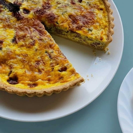 Close up of Smoked Duck and Leek Quiche on a white plate with a slice removed showing creamy interior with smoked duck and leeks, 24cm family size, Carpina Bakery Singapore