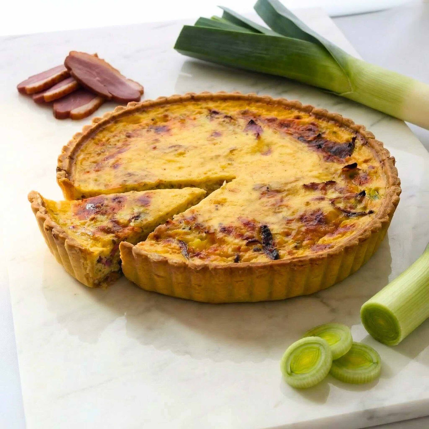 Smoked Duck and Leek Quiche on a round marble board with fresh leeks and smoked duck slices arranged around it, 24cm family size, Carpina Bakery Singapore